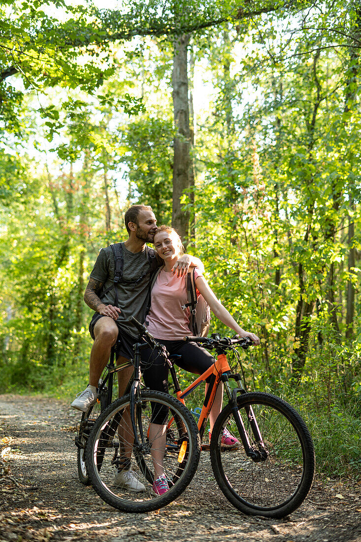 Young man kissing on woman head while standing with bicycles in forest