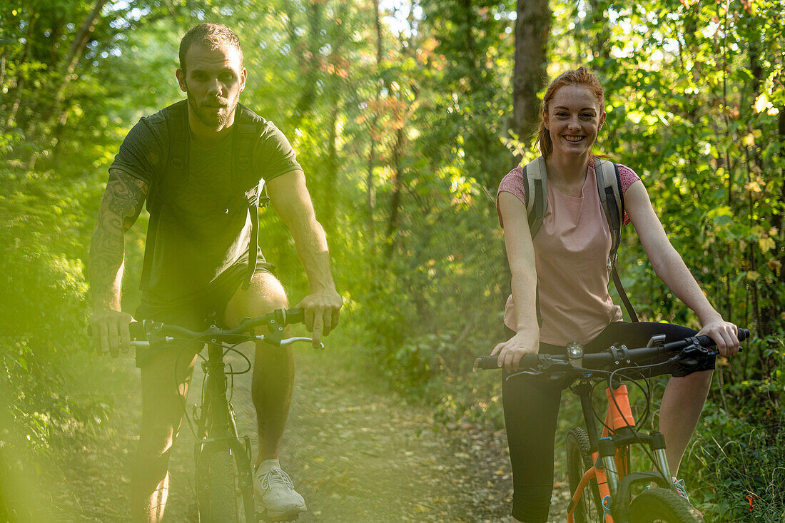 Smiling young couple cycling in forest