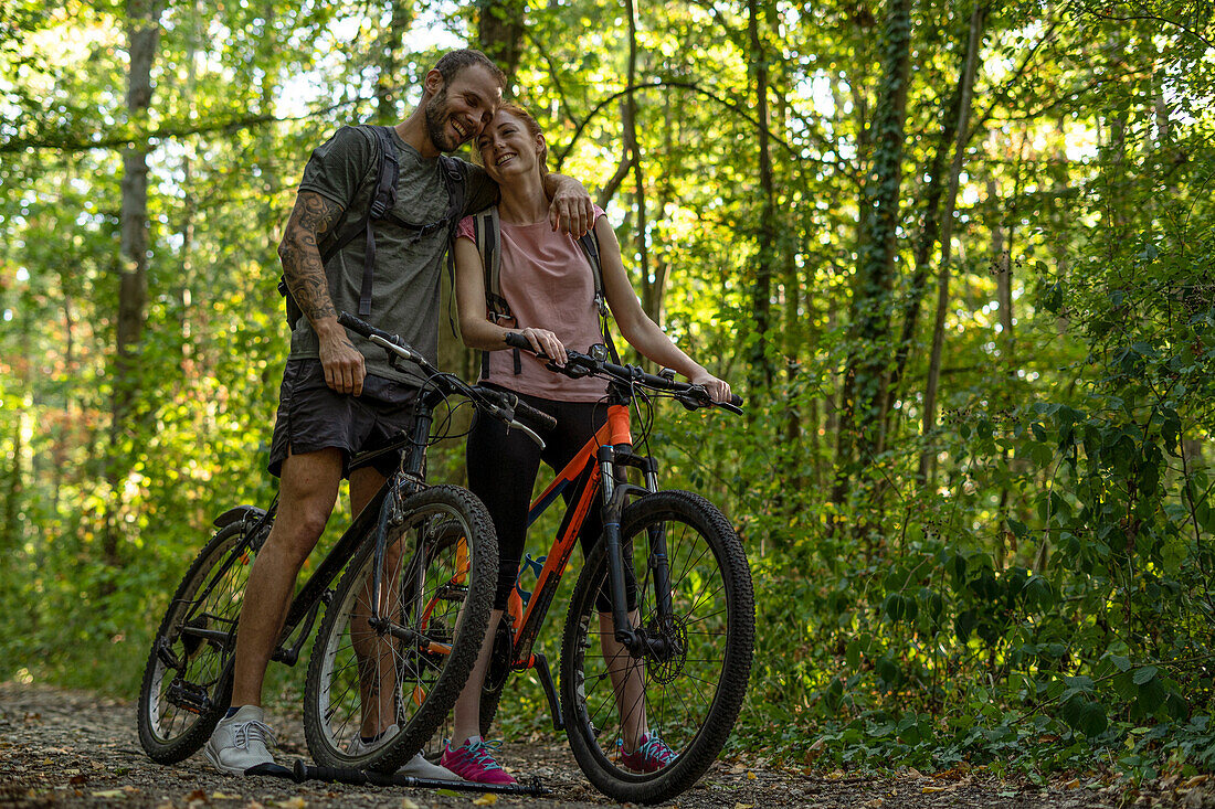 Smiling young couple standing with bicycles in forest