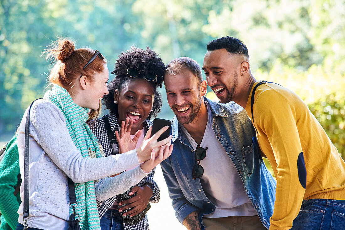 Glückliche junge Freunde, die ein Smartphone in einem öffentlichen Park benutzen