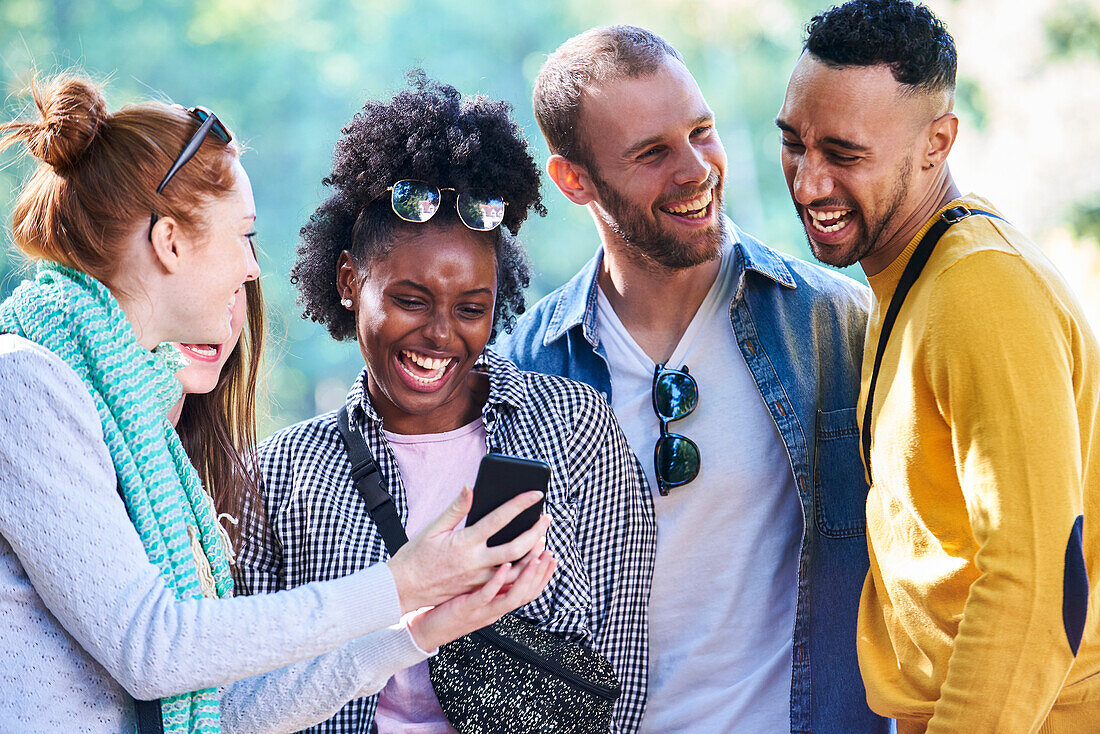 Glückliche junge Freunde, die ein Smartphone in einem öffentlichen Park benutzen