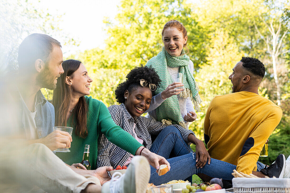 Lächelnde junge Freunde, die zusammen in einem öffentlichen Park sitzen