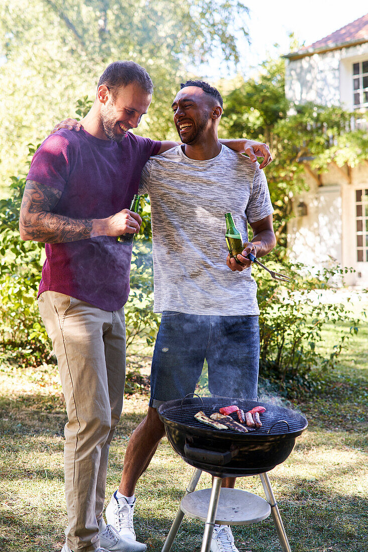 Young men with beer bottles standing near barbecue grill