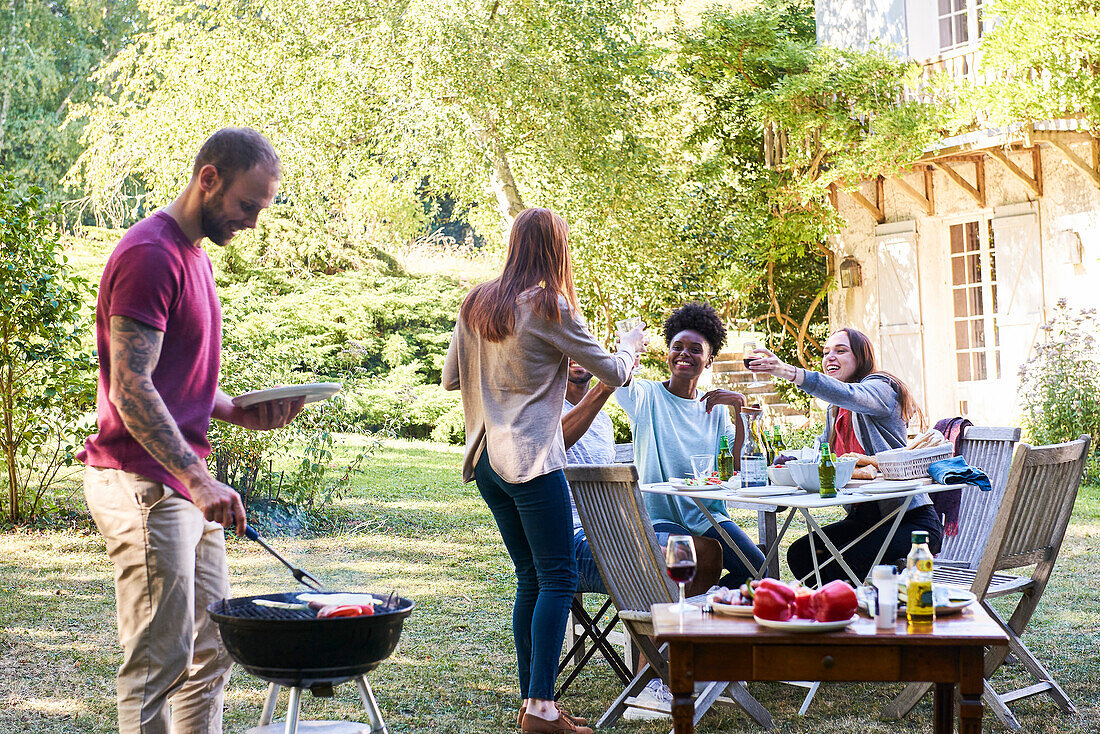 Junger Mann, der mit seinen Freunden am Tisch sitzend Essen im Grill zubereitet