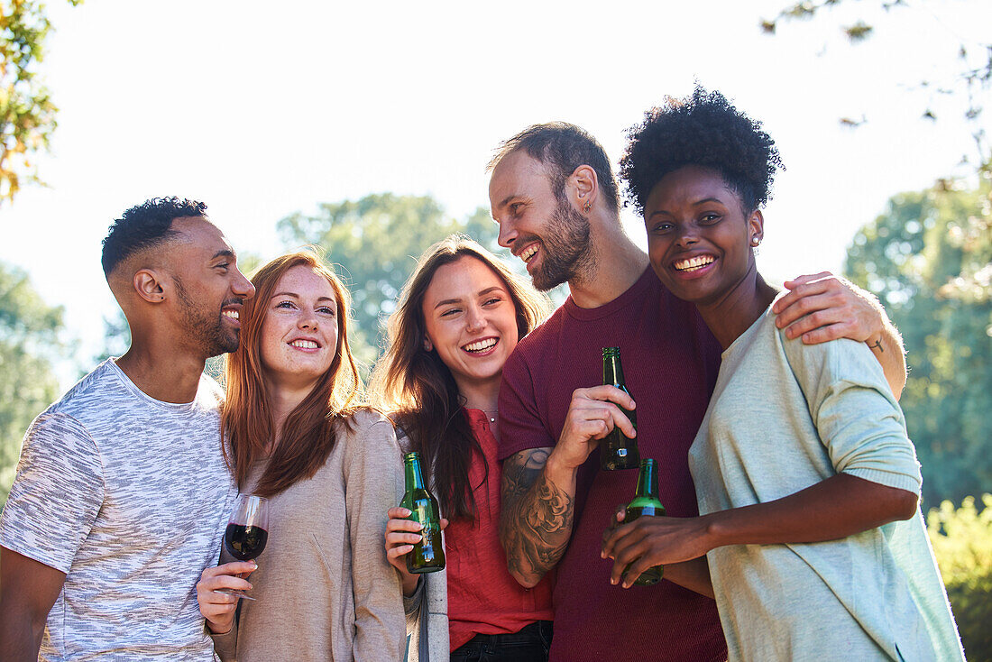 Lächelnde junge Freunde stehen mit Bierflaschen und Weingläsern im Garten