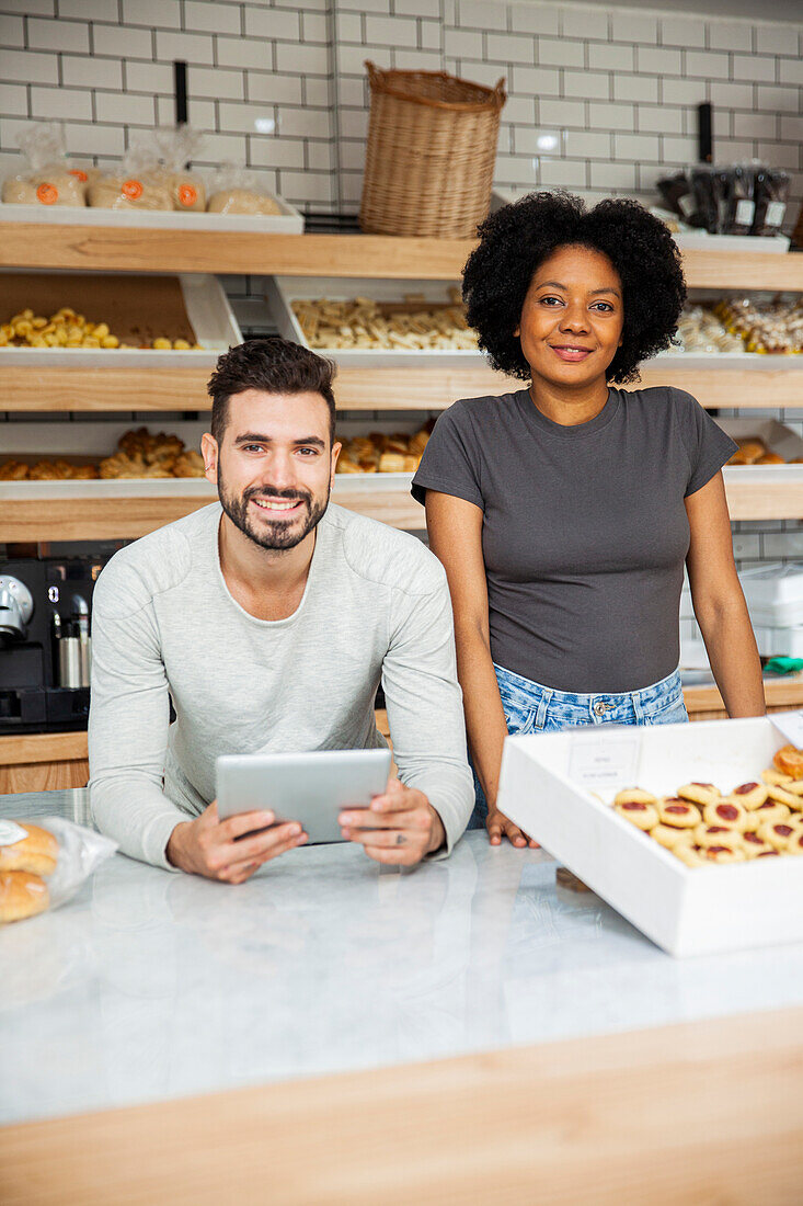 Bakery coworkers standing behind counter while holding digital tablet