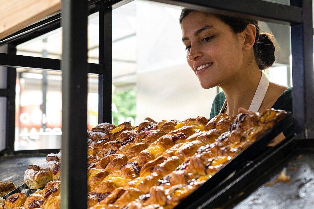 Mittlere Einstellung einer lateinamerikanischen Bäckereibesitzerin mit Blick auf ihre Backwaren in einem Regal