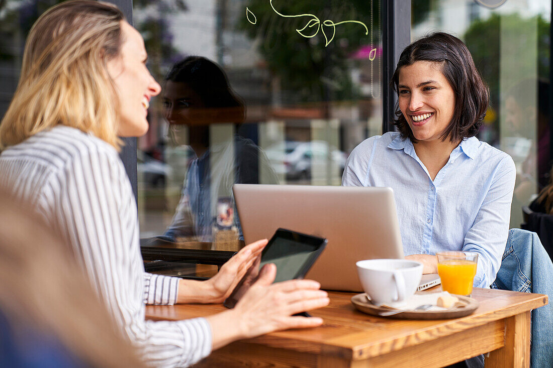 Mittelaufnahme von zwei lächelnden Mitarbeiterinnen, die ihre Arbeit in einem Büro im Freien genießen