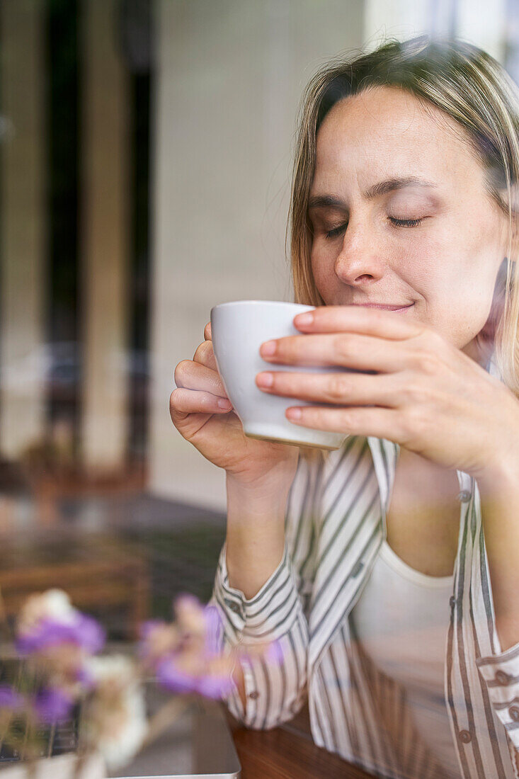 Portrait of attractive woman holding cup of coffee in her hands with eyes closed
