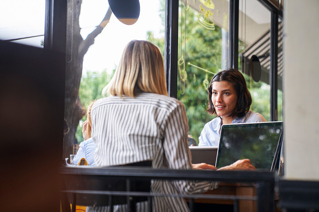 Mid-shot of two female entrepreneurs discussing business while working at cafe