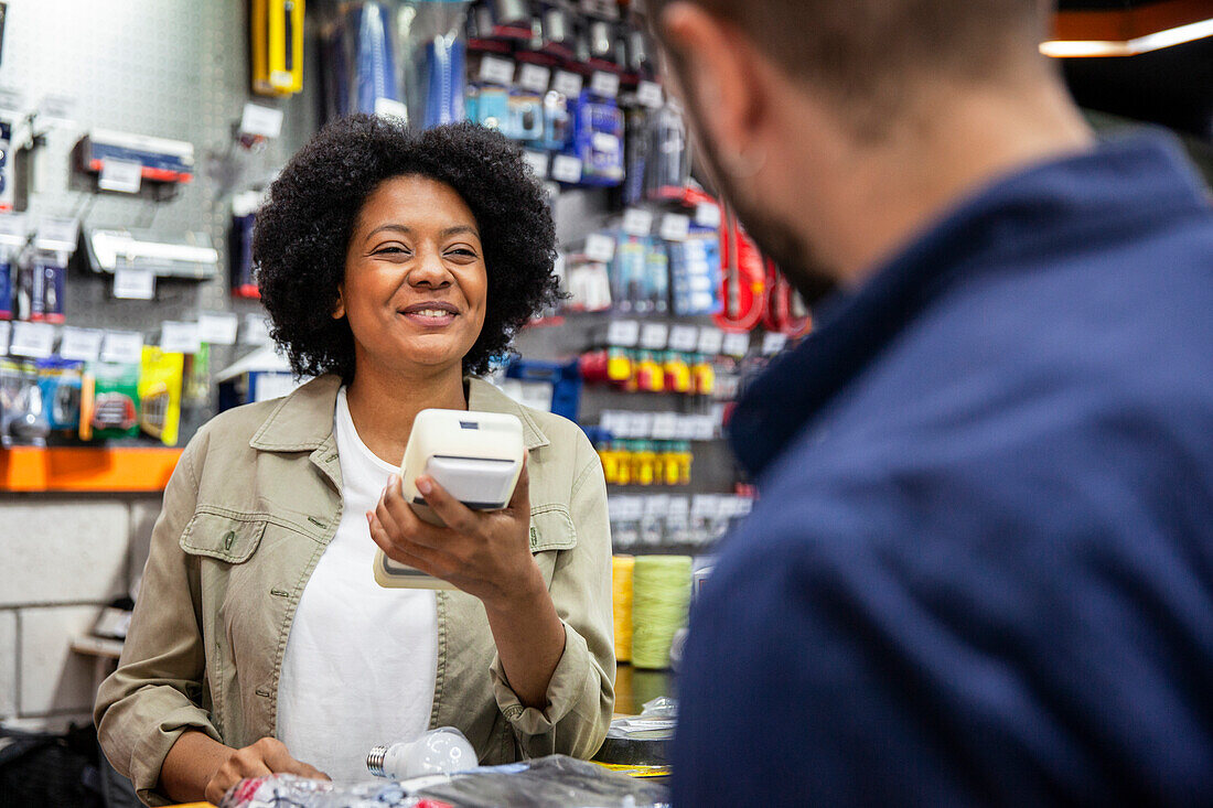 Cheerful African American hardware shop worker talking with male customer