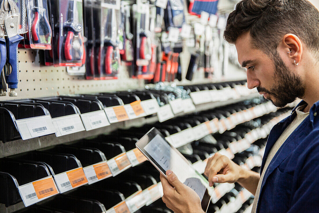 Male hardware shop worker taking inventory on digital tablet