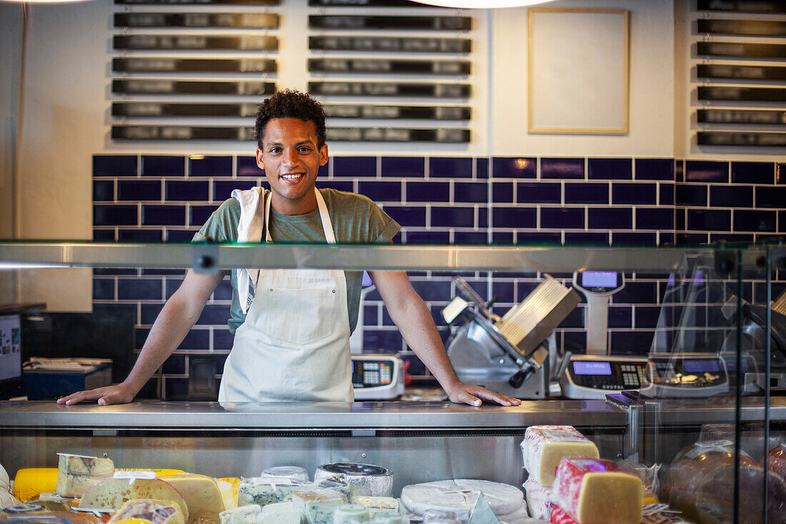 Smiling Latin American young man standing behind counter in cheese store