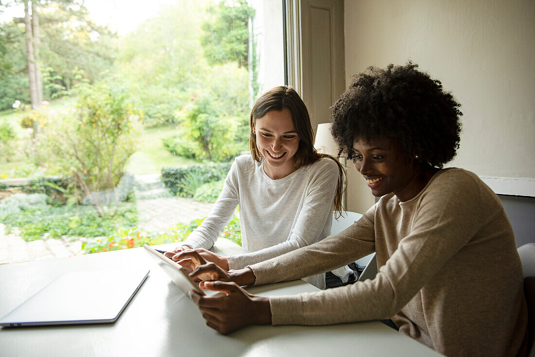 Lächelnde junge Frauen, die zu Hause ein digitales Tablet benutzen