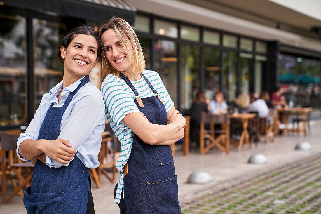Porträt von zwei glücklichen Restaurantbesitzerinnen, die vor ihrem Restaurant posieren und Spaß haben