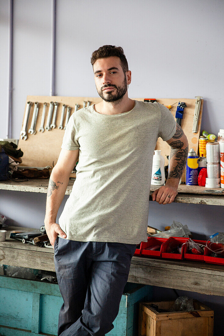 Young adult male mechanic leaning on workbench