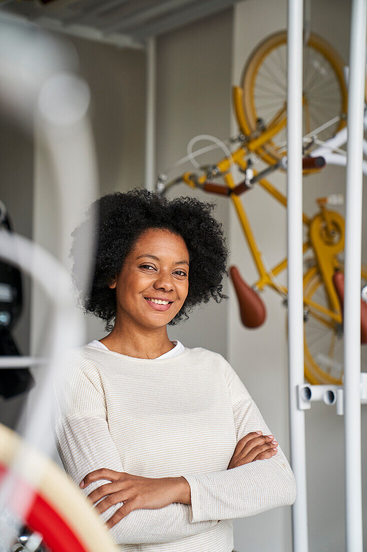 Porträt einer afroamerikanischen Unternehmerin, die in ihrem Fahrradladen posiert, umgeben von Fahrrädern
