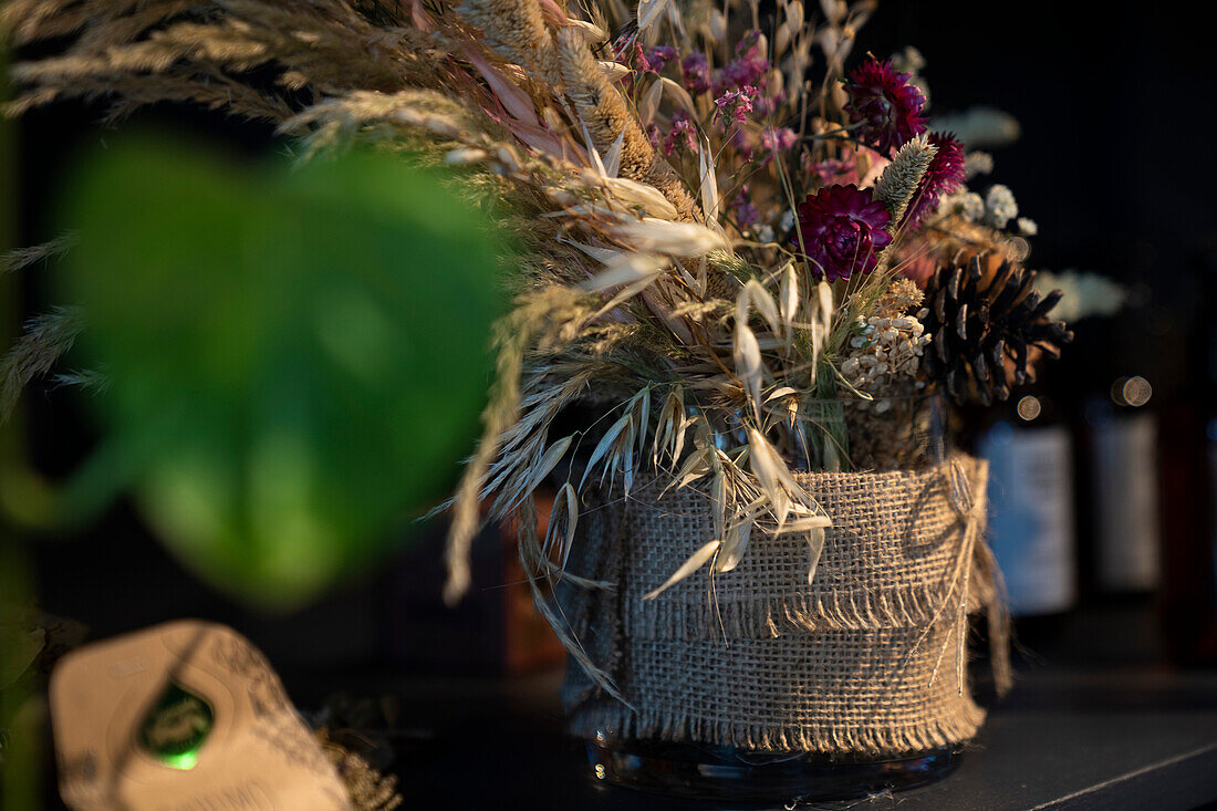 Blumenstrauß aus Trockenblumen in einer Vase, eingewickelt in Sackleinen