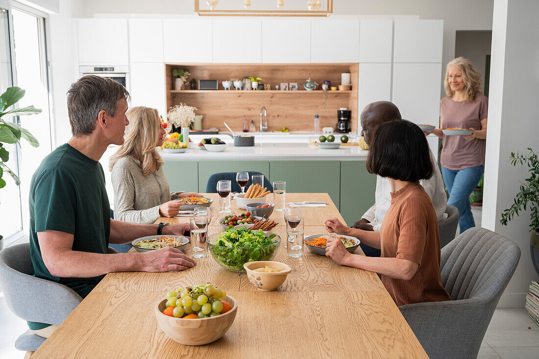 Eine Gruppe von Freunden mittleren Alters versammelt sich zum Abendessen in der Küche