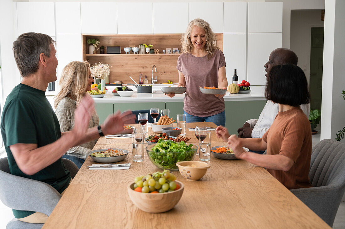 Gruppe älterer Freunde, die sich amüsieren und eine gemeinsame Mahlzeit zu Hause genießen