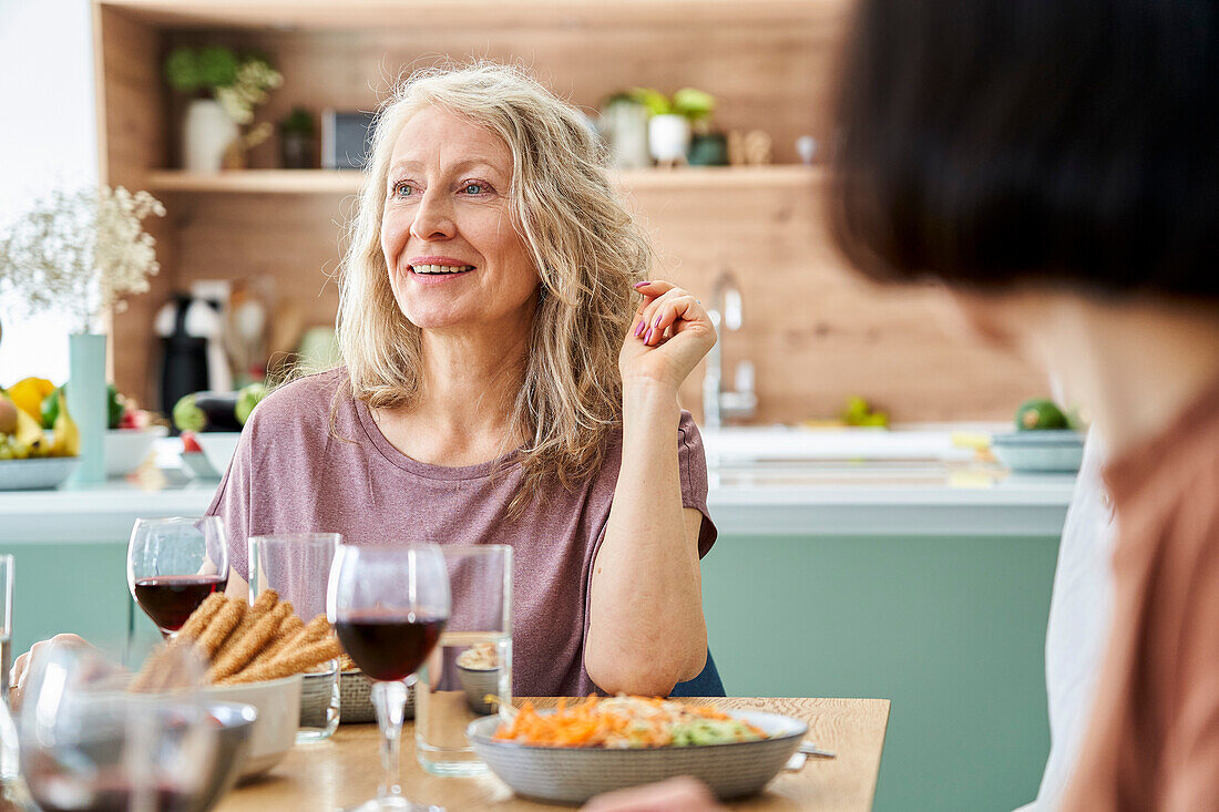 Mid-shot of mature woman sitting at table enjoying meal with friends