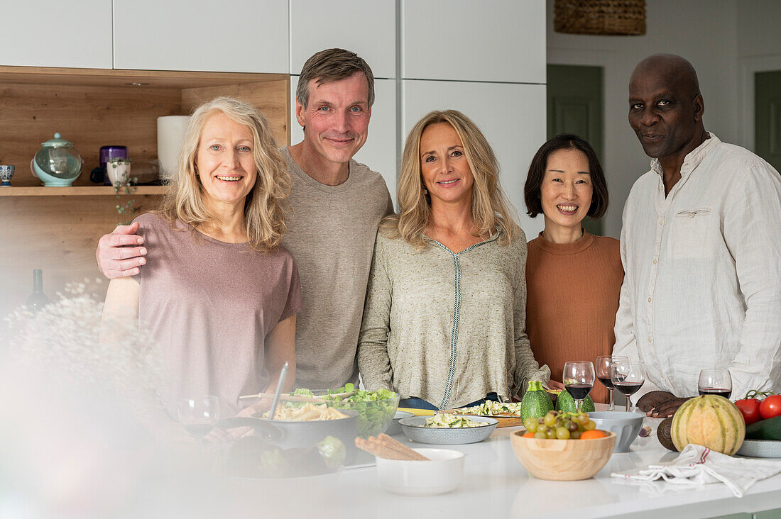 Gruppenporträt von verschiedenen älteren Freunden, die nach dem Kochen an der Kücheninsel stehen