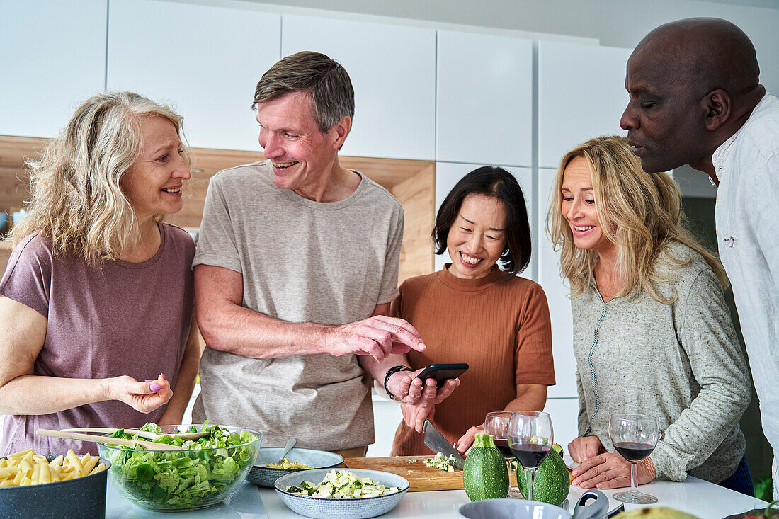 Verschiedene Gruppen von älteren Freunden in der Küche, die ein Smartphone benutzen