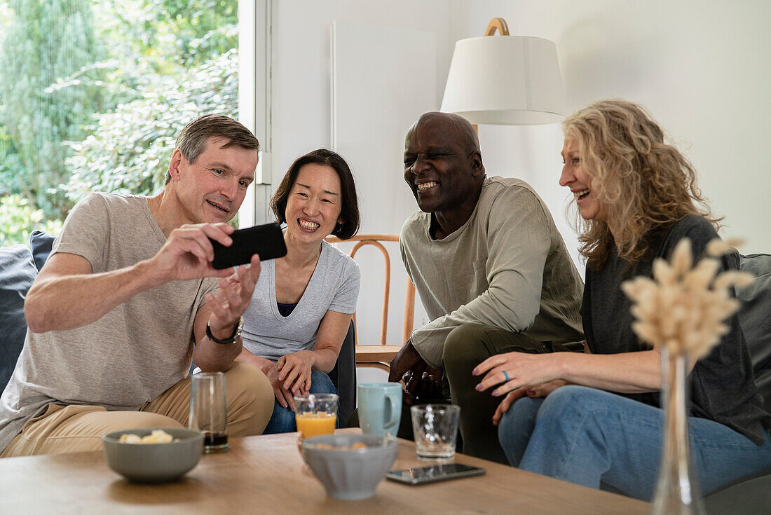 Älterer Mann, der auf dem Sofa sitzend Bilder auf seinem Smartphone mit seinen Freunden teilt