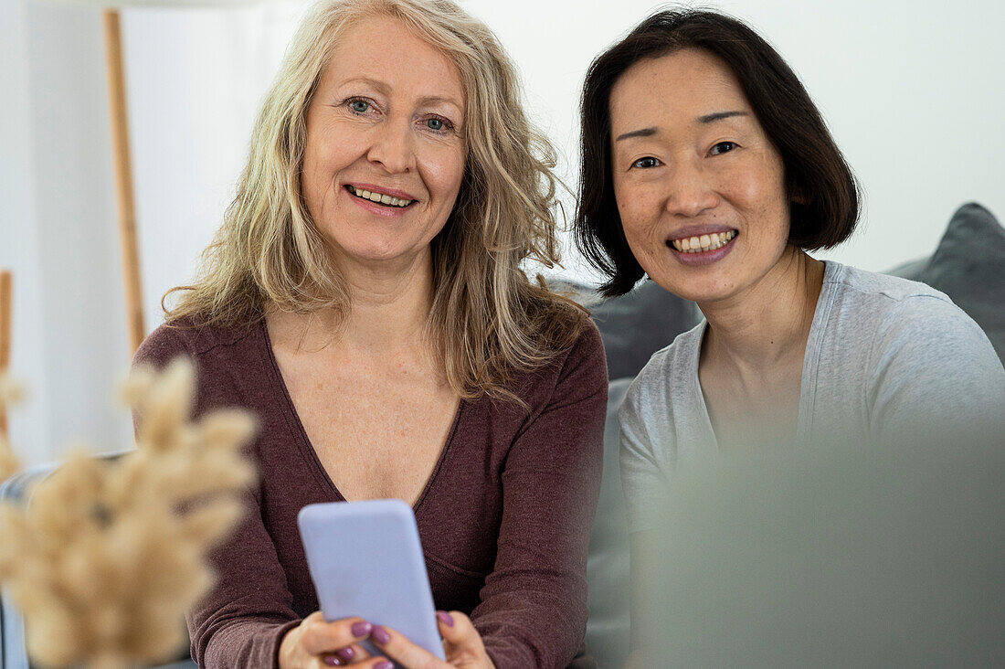 Portrait of two senior female friends looking at camera while having a good tme together at home