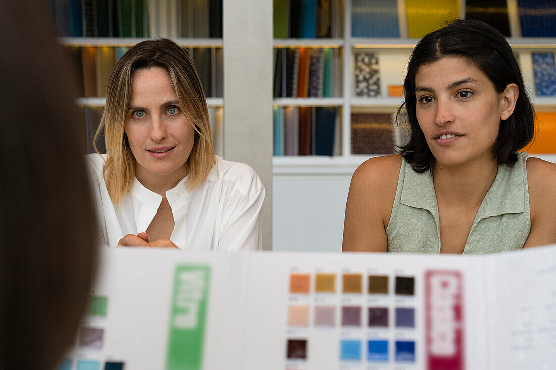 Medium shot of two diverse female interior designers interviewing a client at their studio
