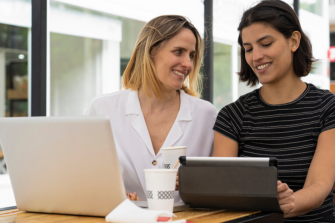 Mittlere Einstellung von zwei Unternehmerinnen, die mit einem Laptop und einem digitalen Tablet arbeiten