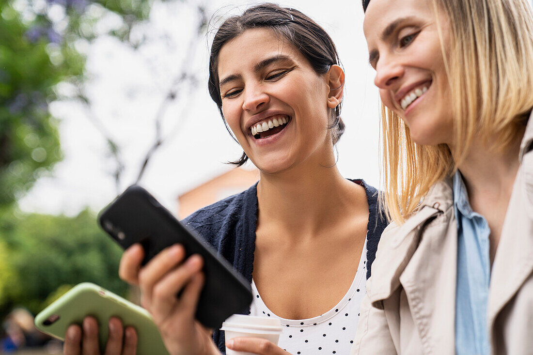 Low angle side view of two female digital nomads having fun with content found on their social media