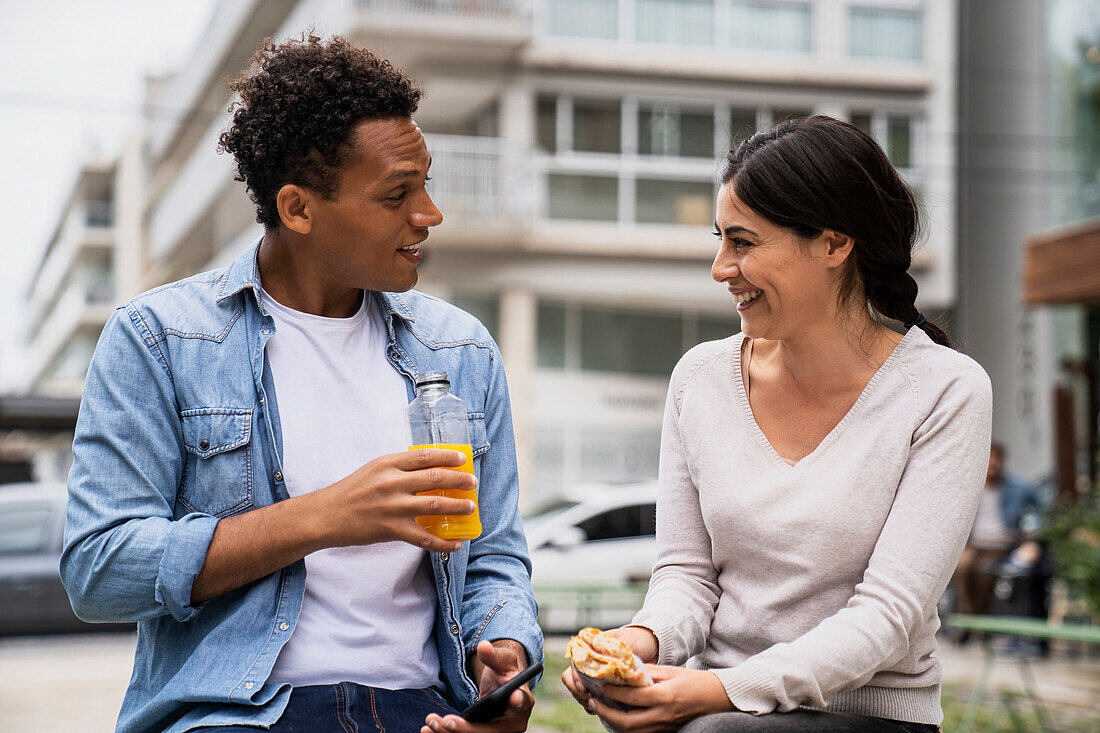 Young African-American man and Latin-American woman having a snack outdoors and enjoying themselves