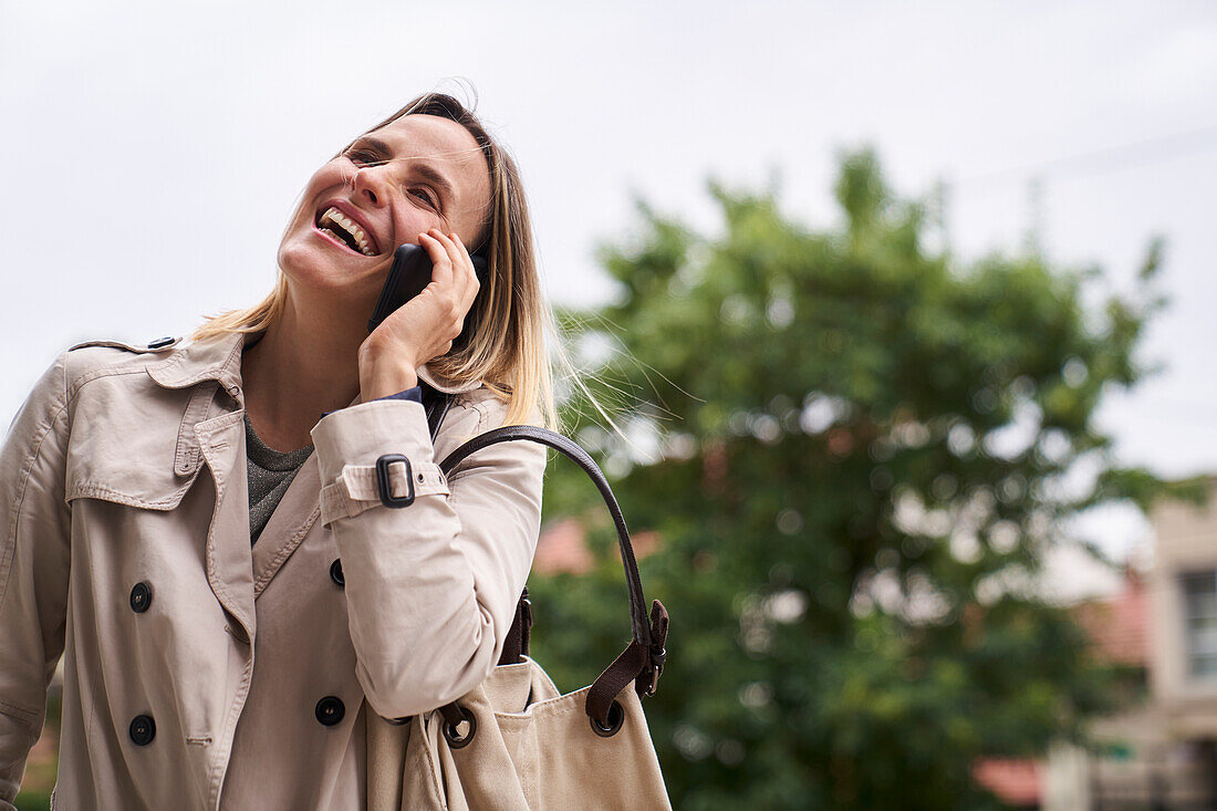 Lächelnde Frau, die mit ihrem Handy spricht, während sie auf der Straße geht