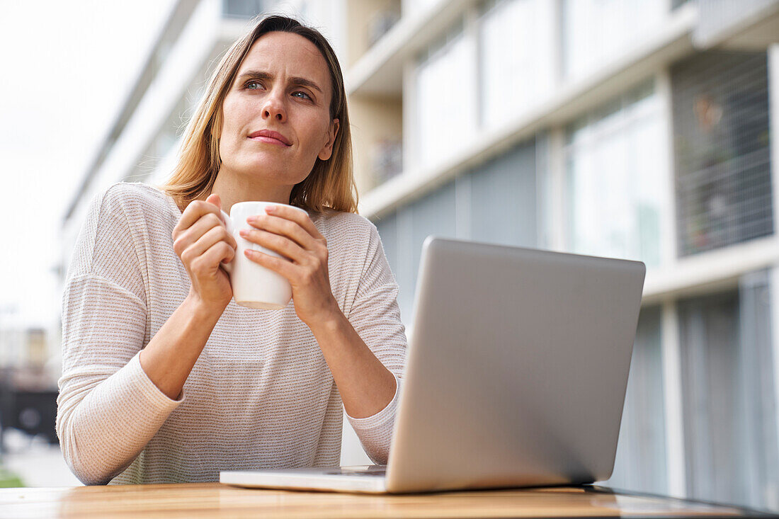 Niedriger Blickwinkel auf eine Unternehmerin, die mit einem Laptop arbeitet und Kaffee trinkt