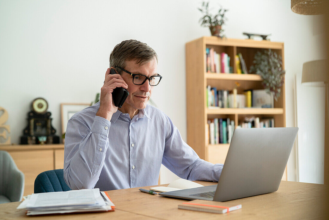 Älterer Geschäftsmann, der im Home-Office die Voicemail auf seinem Smartphone abhört
