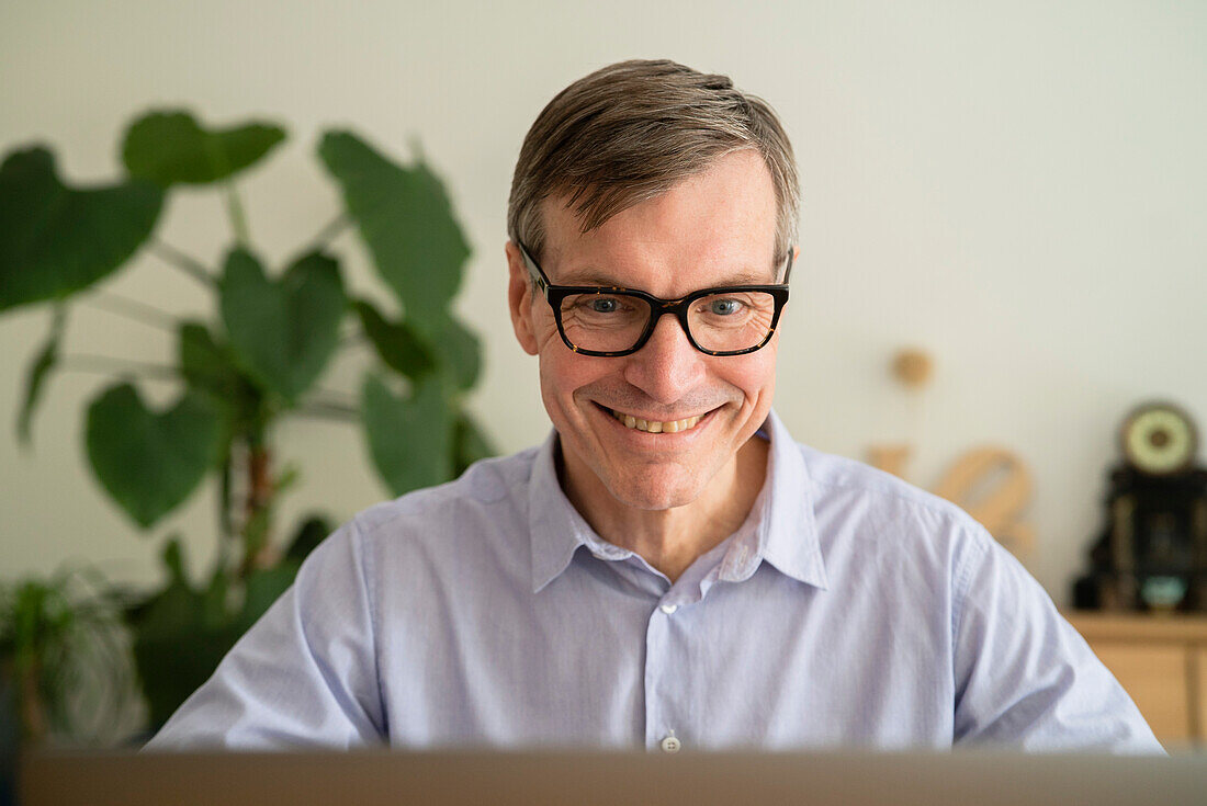 Älterer Mann lächelt, während er zu Hause einen Laptop benutzt
