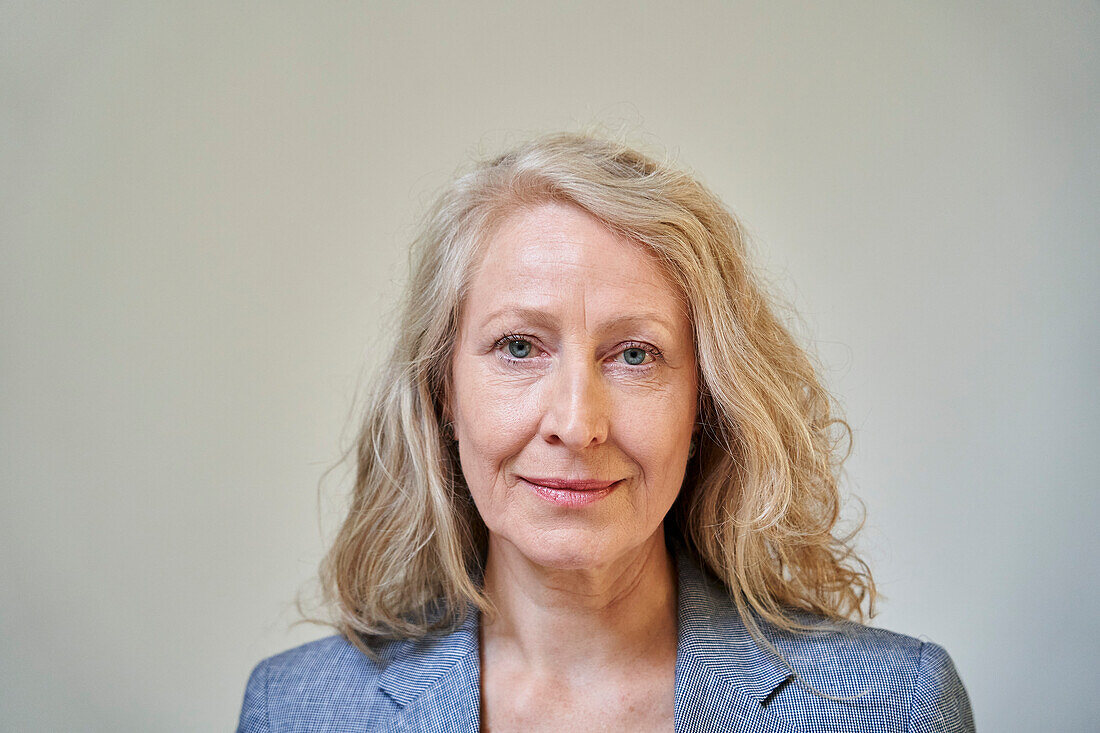 Senior blonde woman looking at the camera while standing against white background