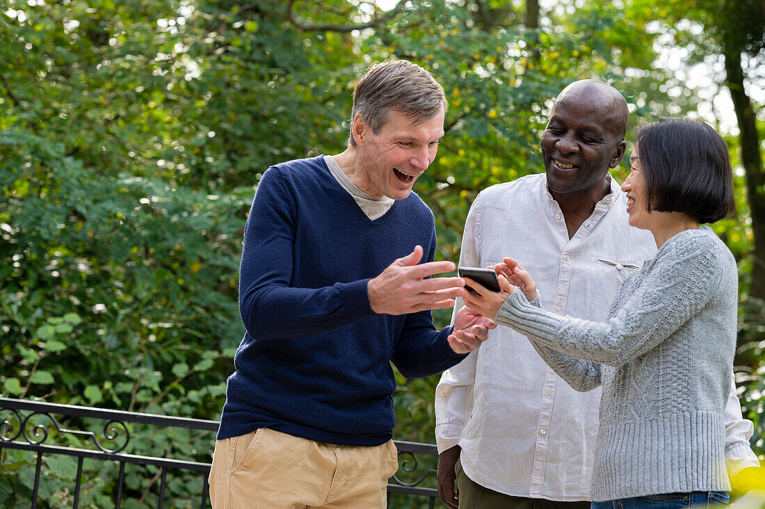 Portrait of three friends looking at cellphone's screen while hanging out outdoors in public park