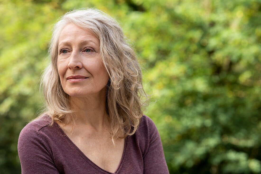 Porträt einer älteren Frau, die im Freien in ihrem Garten sitzt