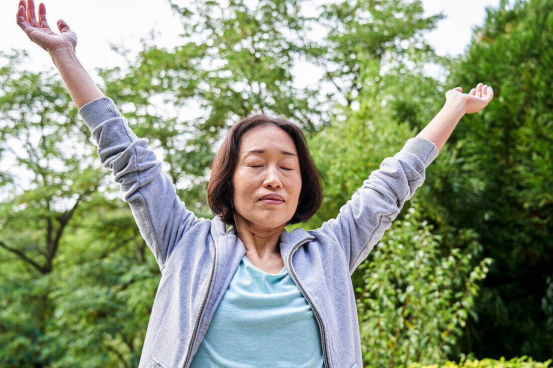 Senior Asian woman stretching while raising arms