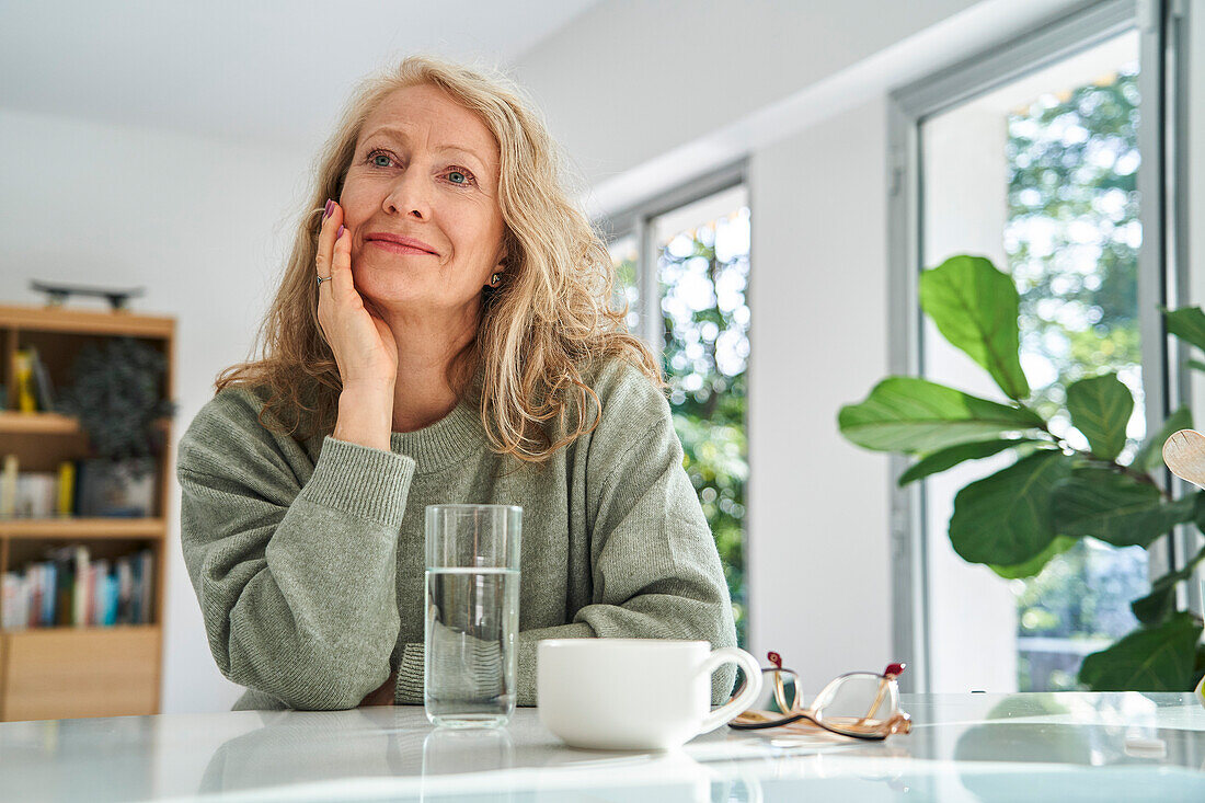 Smiling senior woman looking up while sitting with hand on chin