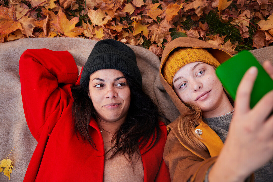 Freunde machen ein Selfie, während sie auf dem Boden liegen, in einer Herbstlandschaft