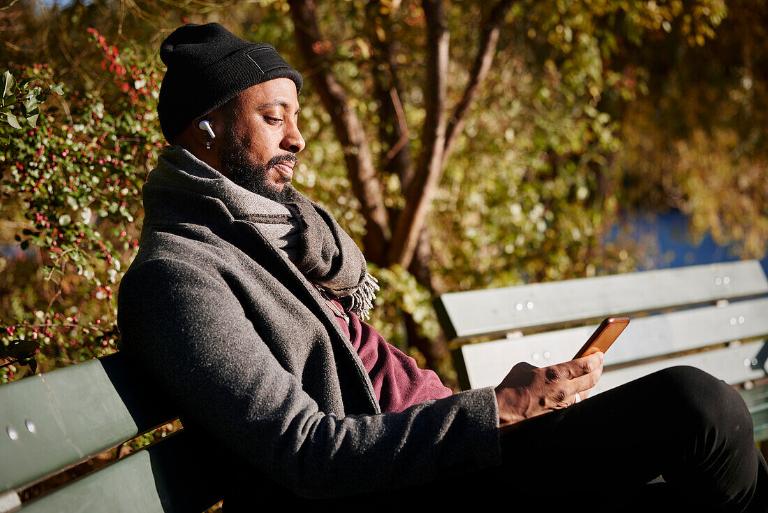 Man sitting on bench and using phone in autumn park