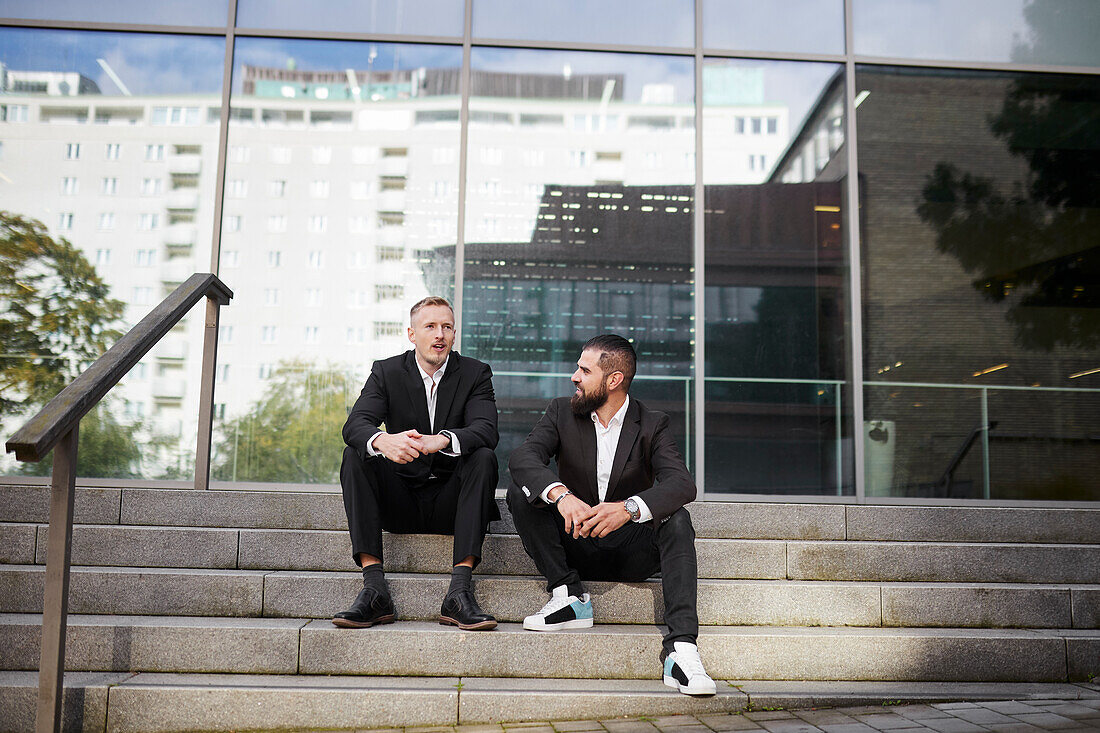Geschäftsleute sitzen auf einer Treppe außerhalb eines Bürogebäudes