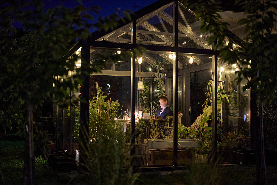 Woman sitting in illuminated greenhouse