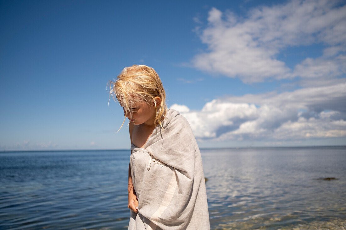Blond girl wrapped in towel on beach