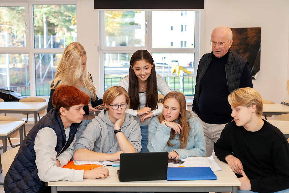 Teenage kids and teacher using laptop in classroom