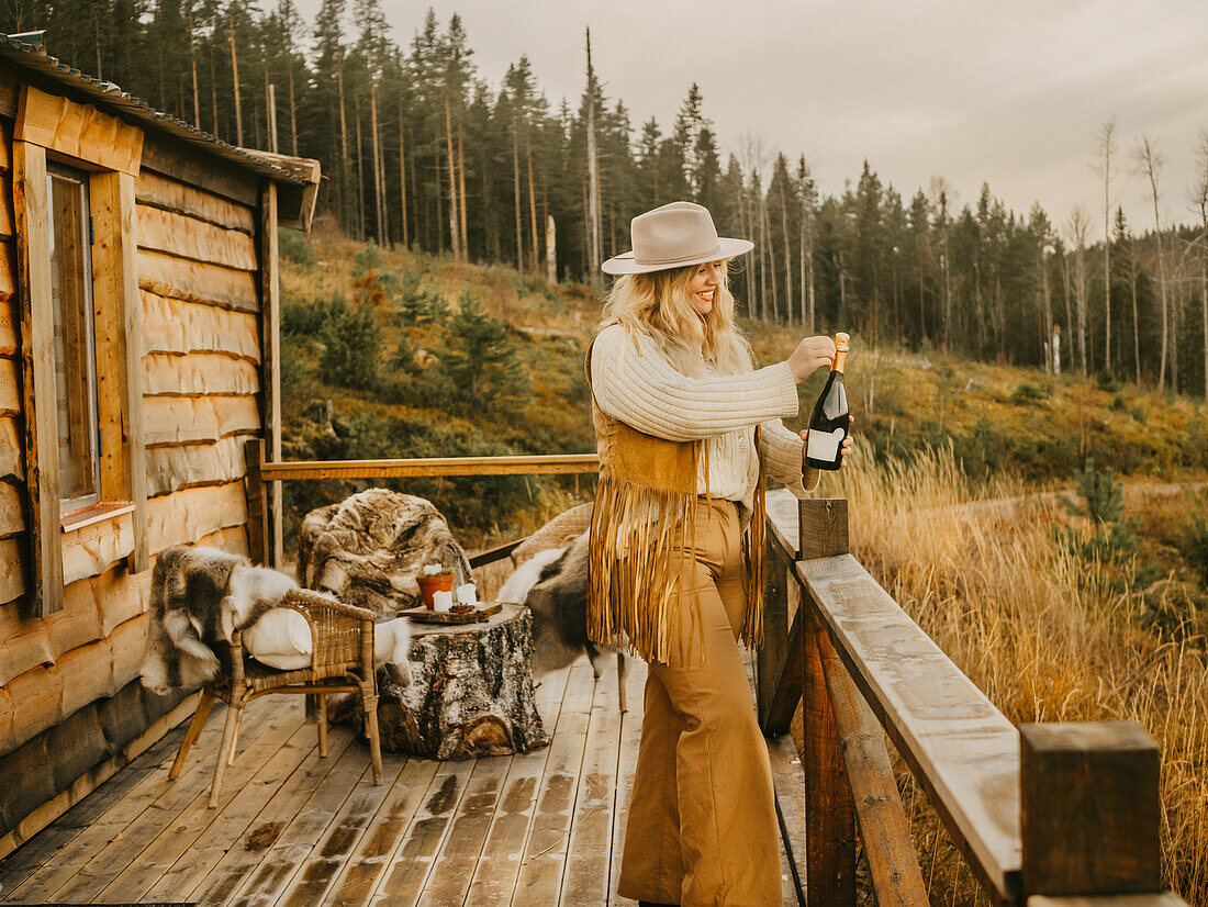 Smiling woman on terrace opening champagne