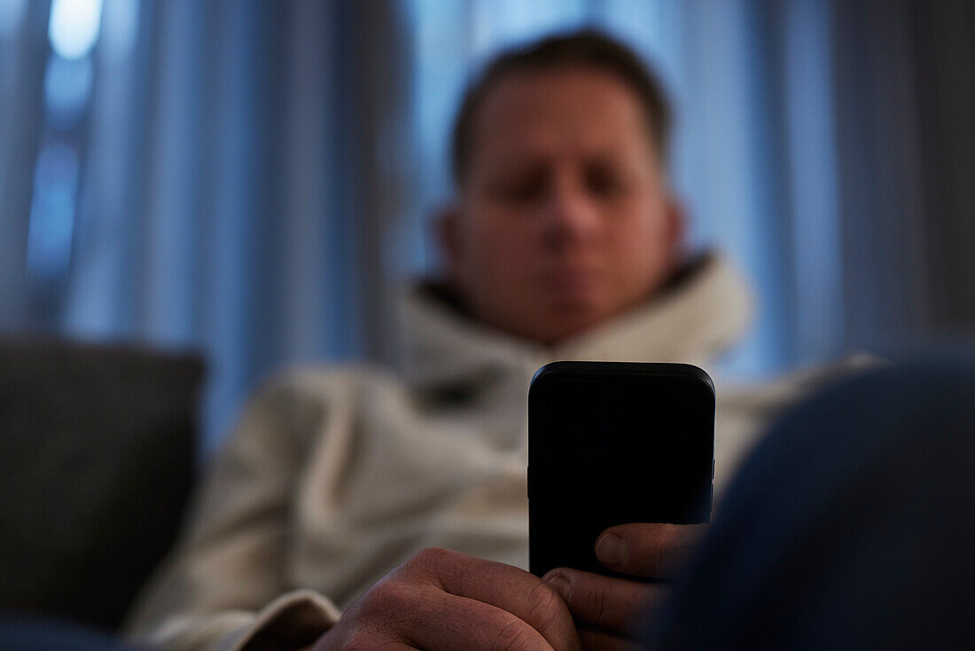 Kranker Mann auf dem Sofa sitzend mit Smartphone
